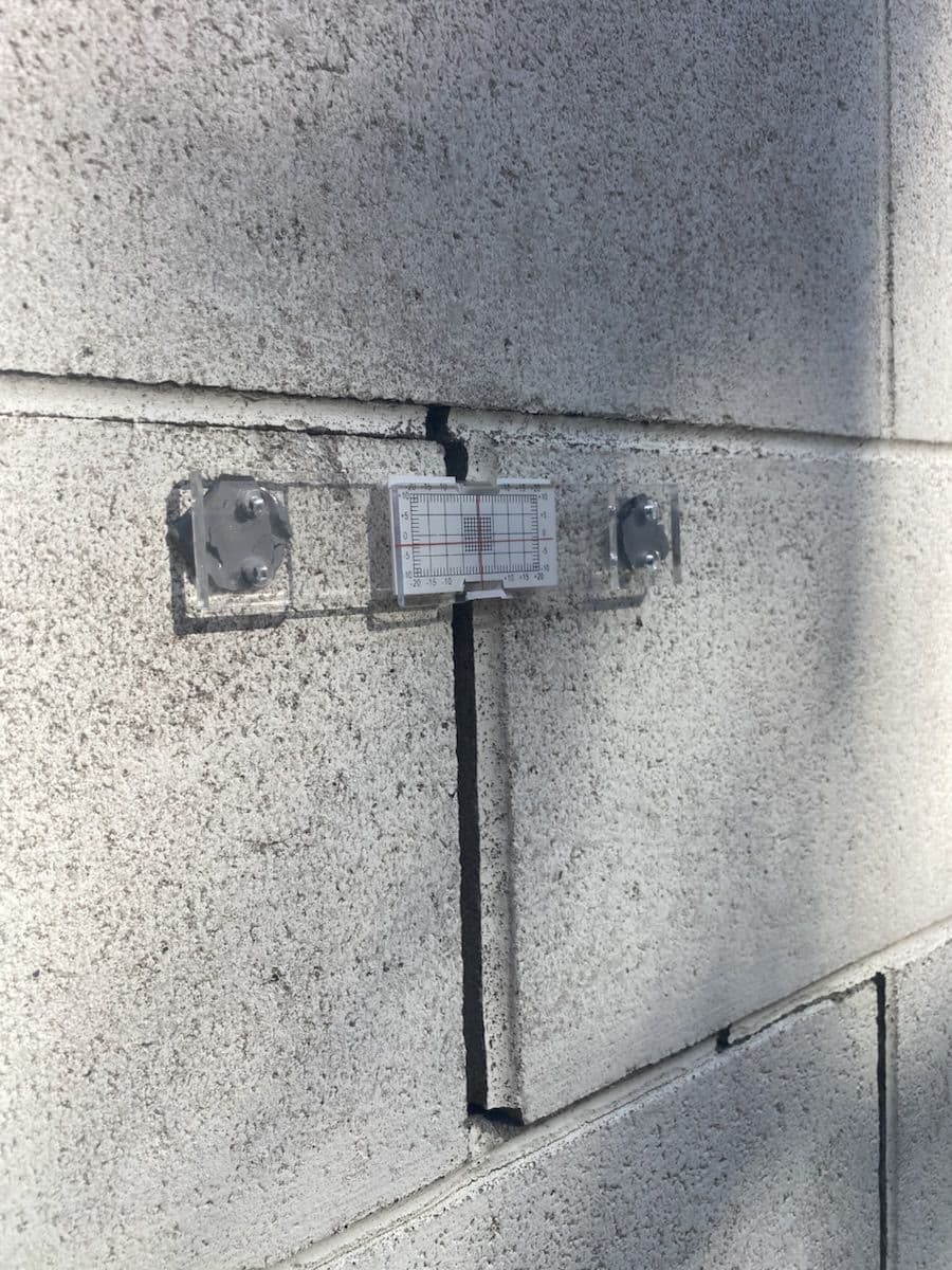 Close view of the tell-tale gauge fitted across the same concrete-block crack