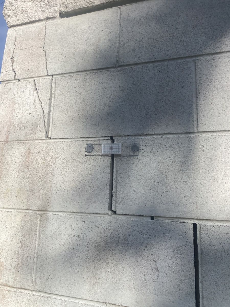 Wide view of a concrete-block wall, showing a crack and tell-tale gauge in context